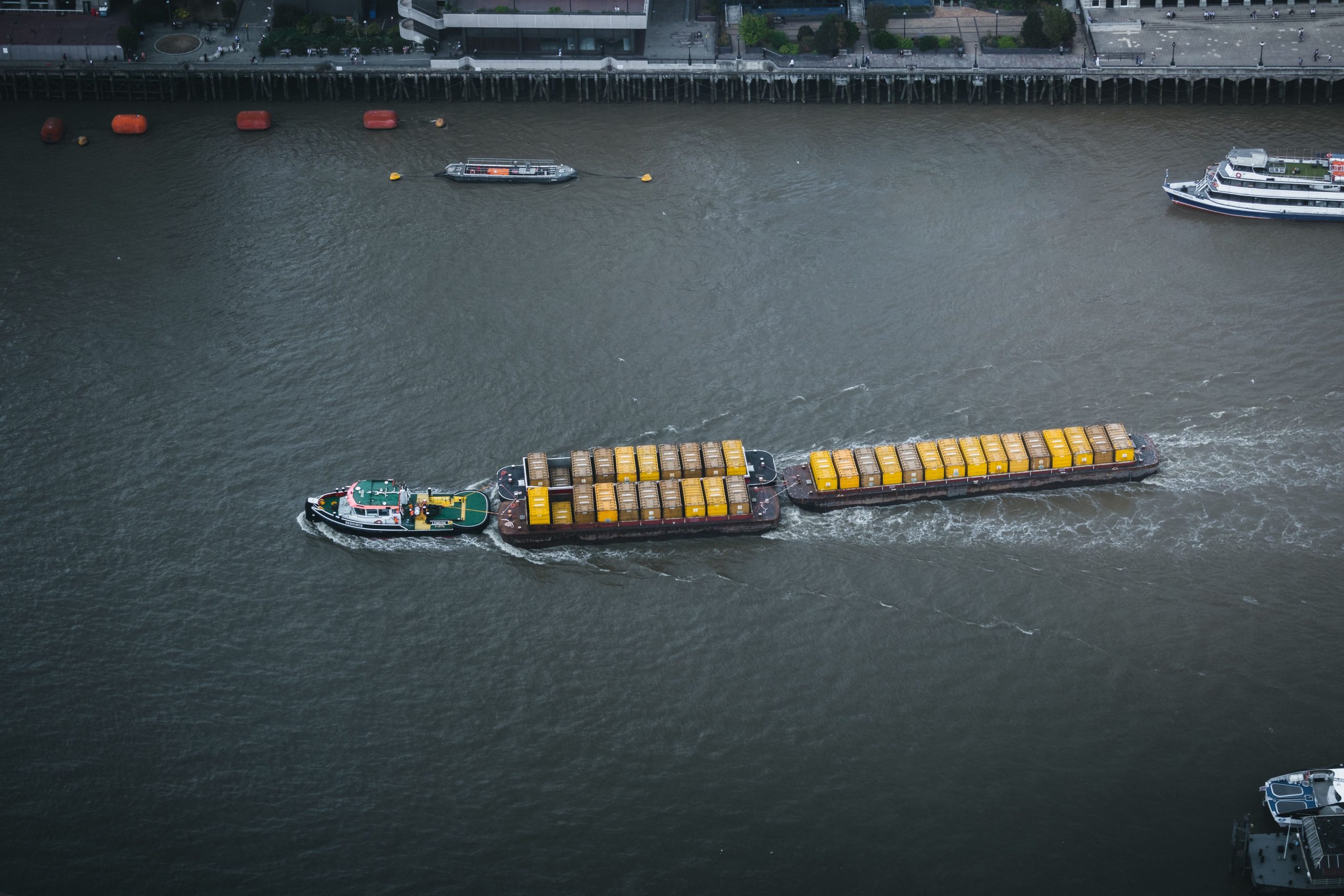 Aerial shot of a tugboat pulling cargo on the Thames River in London, England. Urban background.